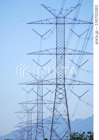 High-voltage power lines and transmission towers against a clear blue sky, illustrating electrical infrastructure and energy transport. 130702881