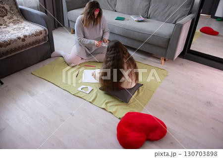 A mother and daughter spend quality time together, creating art on the floor. They are focused and engaged in a shared creative activity. A mother and daughter spend quality time together, creating art on the floor. They are focused and engaged in a shared creative activity. 130703898