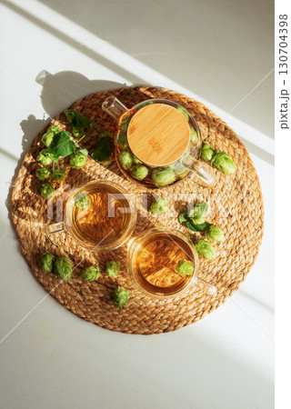 Hop Tea in Glass Teapot and Cups on Woven Placemat. Top View 130704398