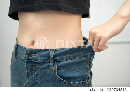 Young Asian woman losing weight wearing loose pants in oversize jeans. 130704811