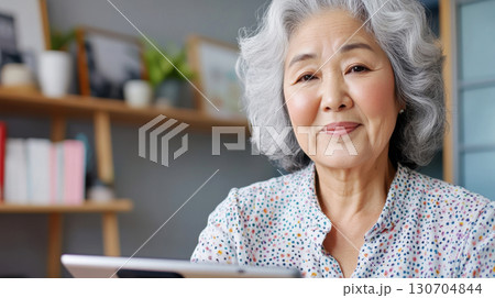 Older Asian woman in a bright office corner holding a tablet answering survey questions for an elegant composition. Survey research answer checklist Older Asian woman in a bright office corner holding a tablet answering survey questions for an elegant composition. Survey research answer checklist 130704844