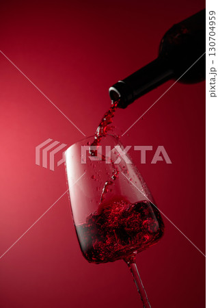 Pouring red wine from a bottle into a glass. Pouring red wine from a bottle into a glass. 130704959
