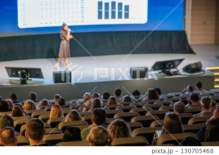 Professional speaker on stage presenting to a seated audience in auditorium Professional speaker on stage presenting to a seated audience in auditorium 130705468