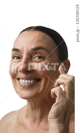 Mature woman smiling while applying cream under eye Mature woman smiling while applying cream under eye 130706529
