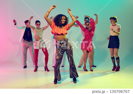 Confident woman in bright top dancing in front of diverse retro group 130706707