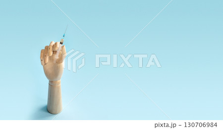 Wooden human hand with syringe with vaccine for disease on light blue background. Doctor holds syringe with medical injection. Health care and disease prevention concept, banner 130706984