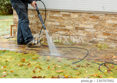 Man cleaning street with high pressure power washer, washing stone garden paths. High quality photo 130707002