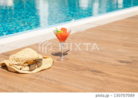 Fresh red cocktail with ice in glass, beach hat and sunglasses on swimming pool. Tropical juice on luxury vacations. Concept summer holiday and travel. High quality photo Fresh red cocktail with ice in glass, beach hat and sunglasses on swimming pool. Tropical juice on luxury vacations. Concept summer holiday and travel. High quality photo 130707089