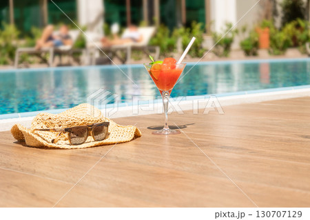 Fresh red cocktail with ice in glass, beach hat and sunglasses on swimming pool. Tropical juice on luxury vacations. Concept summer holiday and travel. High quality photo 130707129