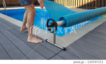 Man covers swimming pool with cover for protection against dirt, leaves, heating and cooling water. 130707151