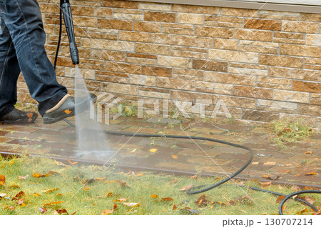 Man cleaning street with high pressure power washer, washing stone garden paths. High quality photo 130707214
