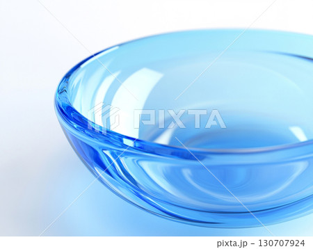 A close-up of a clear, light blue glass bowl on a white surface, showcasing its smooth, translucent surface and a subtle spiral pattern at its base. 130707924