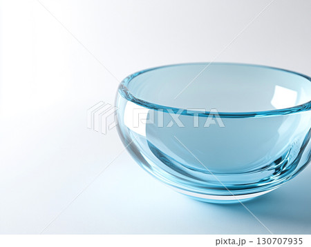 A close-up of a clear, light blue glass bowl on a white surface, showcasing its smooth, translucent surface and a subtle spiral pattern at its base. A close-up of a clear, light blue glass bowl on a white surface, showcasing its smooth, translucent surface and a subtle spiral pattern at its base. 130707935