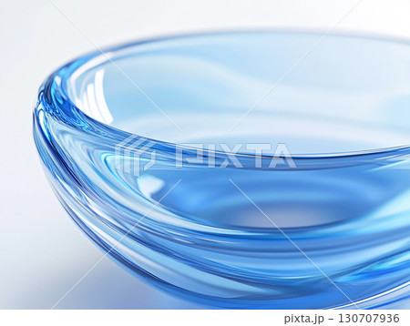 A close-up of a clear, light blue glass bowl on a white surface, showcasing its smooth, translucent surface and a subtle spiral pattern at its base. 130707936