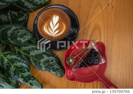 Hot coffee latte with latte art milk foam in cup and Blueberry Cake on wood desk on top view. As breakfast In a coffee shop at the cafe,during business work concept Hot coffee latte with latte art milk foam in cup and Blueberry Cake on wood desk on top view. As breakfast In a coffee shop at the cafe,during business work concept 130709766