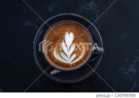 Hot coffee latte with latte art milk foam in cup mug on black wood desk on top view. As breakfast In a coffee shop at the cafe,during business work concept 130709769