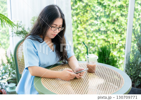 a portrait of beautiful happy asian woman traveler wearing a beautiful blue dress lifestyle enjoying holding using smartphone cellphone casual working in sitting coffee shop restaurant background 130709771