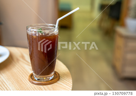Close-up of Iced Black americano in a glass cup mug on wood desk office desk in coffee shop at the cafe in garden,during business work concept Close-up of Iced Black americano in a glass cup mug on wood desk office desk in coffee shop at the cafe in garden,during business work concept 130709778