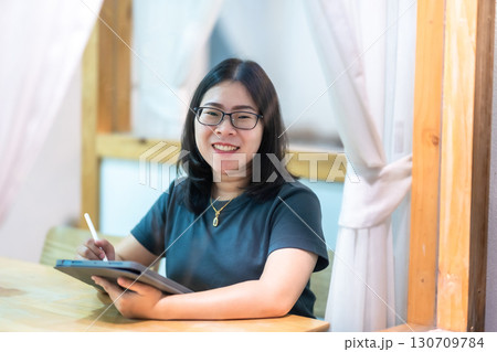 Portrait asian freelance people business female wearing glasses stylish hipster Draw or taking note on digital tablet with electronic pen for browsing internet, chatting and blogging in coffee shop. 130709784