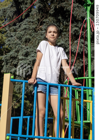 Young girl enjoying time at the playground surrounded by tall evergreen trees 130709949