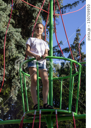 Girl standing on a green play structure surrounded by trees outdoors 130709950