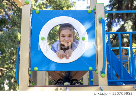 Young girl smiling while playing peek-a-boo on a colorful playground structure Young girl smiling while playing peek-a-boo on a colorful playground structure 130709952