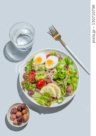 Tuna salad with cherry tomatoes, eggs, olives and cucumbers in a plate on a blue background 130710796
