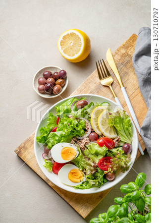 Tuna salad with olives, lettuce, tomatoes, eggs and lemon in a plate on a wooden board Tuna salad with olives, lettuce, tomatoes, eggs and lemon in a plate on a wooden board 130710797