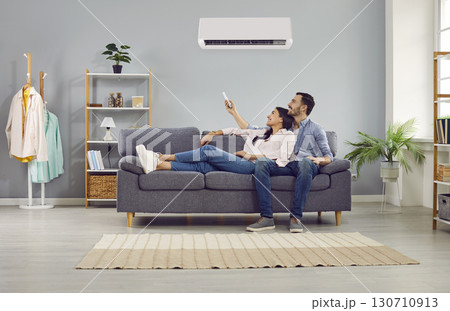 Happy family couple relaxing on the sofa and setting up the temperature on the air conditioner 130710913