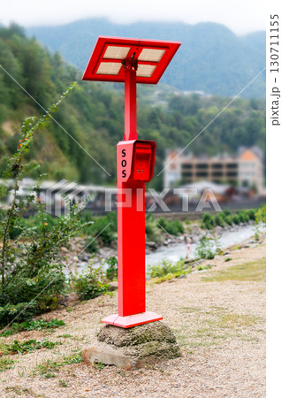 Outdoor bright red SOS emergency call box in environment with river and mountains in the distance, attention to the safety and communication equipment Outdoor bright red SOS emergency call box in environment with river and mountains in the distance, attention to the safety and communication equipment 130711155