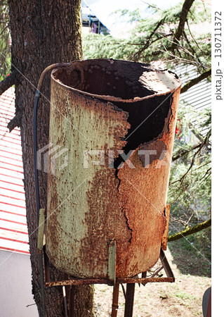 Rusty water tank on a tree stand showcasing decay and weathering in a rural setting Rusty water tank on a tree stand showcasing decay and weathering in a rural setting 130711372