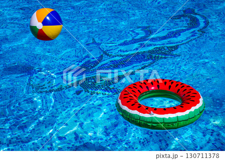 Colorful beach ball and watermelon circle, floating in the pool water, on a sunny summer day, no people 130711378