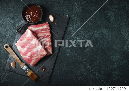 Raw meat. Raw pork ribs from the back with meat on a black background. background image Raw meat. Raw pork ribs from the back with meat on a black background. background image 130711969