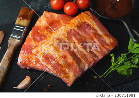 Ready for BBQ raw pork spare ribs with barbecue sauce. Black background. Top view 130711981