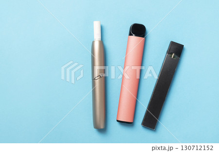 of three different types of vaping devices - a IQOS, a disposable vape, and a pod system on a vibrant blue background. of three different types of vaping devices - a IQOS, a disposable vape, and a pod system on a vibrant blue background. 130712152