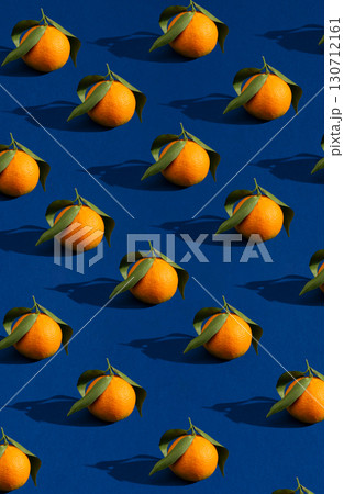 A vibrant, repeating pattern of fresh oranges with green leaves on a bold blue background, casting strong shadows. 130712161