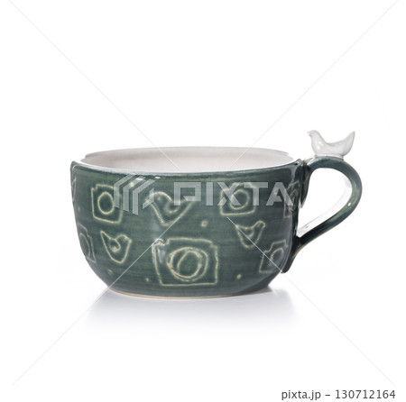 A teal-green ceramic mug with carved patterns of birds and cameras stands on a white background A teal-green ceramic mug with carved patterns of birds and cameras stands on a white background 130712164