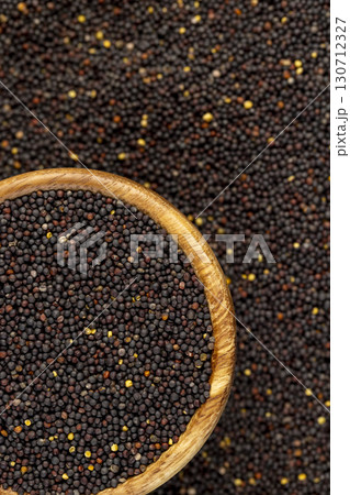 a large number of black rapeseed seeds are used to produce rapeseed oil, round wooden bowl filled with round rapeseed seeds 130712327