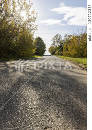 a road in the autumn season, a beautiful bright landscape with a road and yellowing trees in the sunlight a road in the autumn season, a beautiful bright landscape with a road and yellowing trees in the sunlight 130712358