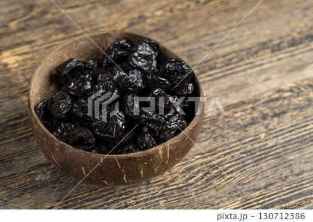black prunes made from ripe blue plums in a coconut shell plate, dried plums in a bowl made from natural materials 130712386
