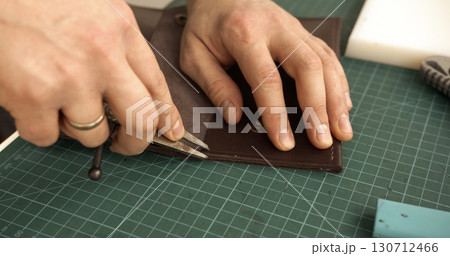 Artisan hands cutting brown leather piece for handmade wallet Artisan hands cutting brown leather piece for handmade wallet 130712466