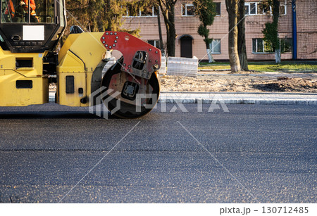 Road roller machine compacts fresh asphalt during street construction on urban roadway, close-up of heavy machinery wheel. Road roller machine compacts fresh asphalt during street construction on urban roadway, close-up of heavy machinery wheel. 130712485
