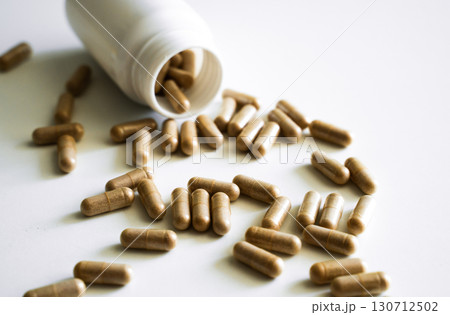 Brown herbal capsules scattered on white background, natural dietary supplement symbolizing organic medicine, healthcare and alternative therapy 130712502