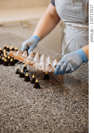Handmade chocolate candies being unmolded at confectionery factory by chocolatier in gloves 130713017