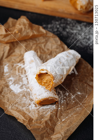 Caramel cream filled pastry rolls dusted with powdered sugar on parchment paper 130713025