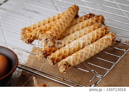 Homemade wafer rolls with nuts on a cooling rack with baking ingredients, rustic setup 130713028