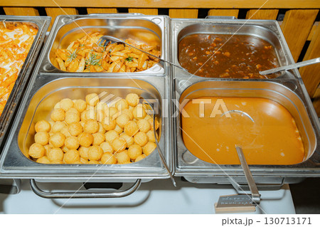 Buffet setup displaying a delicious variety of foods including golden fried balls, roasted wedges, thick stew, and creamy soup, inviting guests to a tasty dining experience Buffet setup displaying a delicious variety of foods including golden fried balls, roasted wedges, thick stew, and creamy soup, inviting guests to a tasty dining experience 130713171