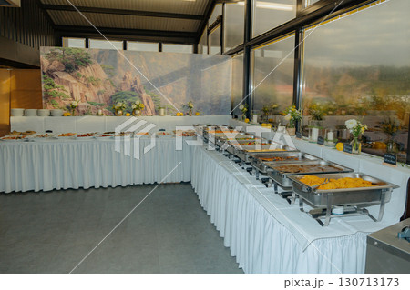 Buffet setup showcases a variety of dishes in warmers and platters, ready for self-service at an event. A decorative backdrop with flowers enhances the elegant dining atmosphere. 130713173