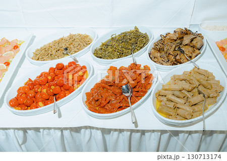 A display of assorted Mediterranean appetizers arranged on a buffet table. Includes colorful dishes like roasted vegetables, stuffed grape leaves, and marinated delicacies, ready to serve 130713174