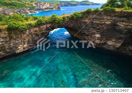 Rock broken by an ocean wave forming an arch in the mountain. Cliff is washed by powerful waves of ocean. Angel's Billabong is a popular tourist destination on the island of Nusa Penida in Indonesia. 130713407